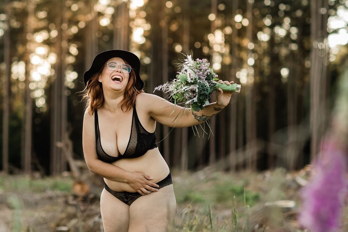 Lachendes Mädchen mit Blumenstrauß in schwarzer Unterwäsche